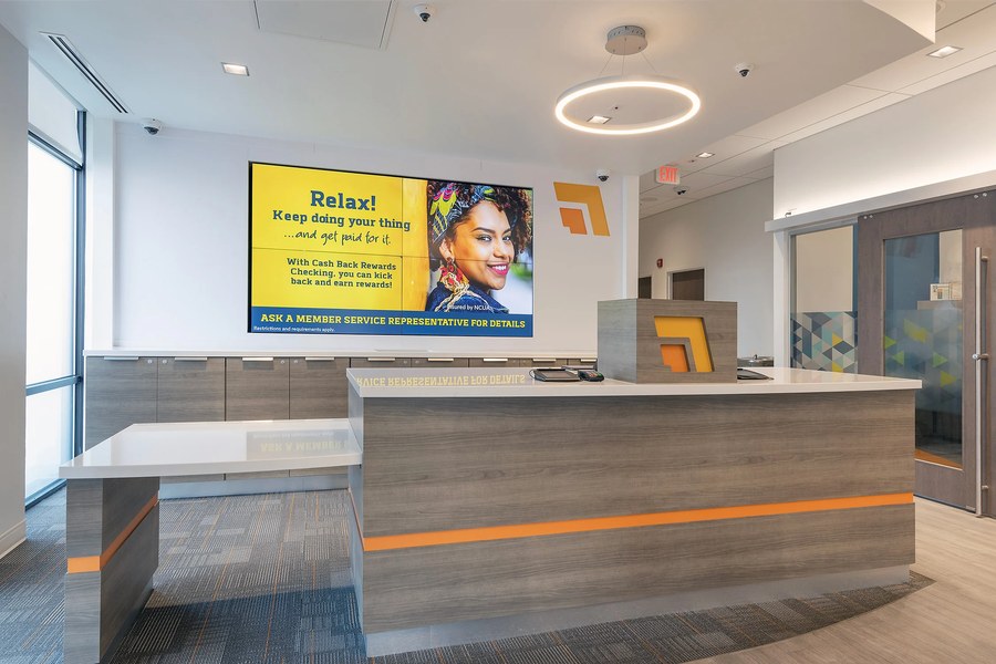 Bank teller line with orange brand accent and digital signage wall by Robertson Cabinets