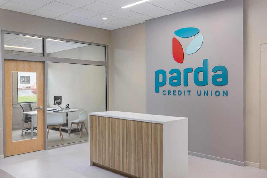 Credit union greeter desk with clean modern millwork and branded signage wall by Robertson Cabinets
